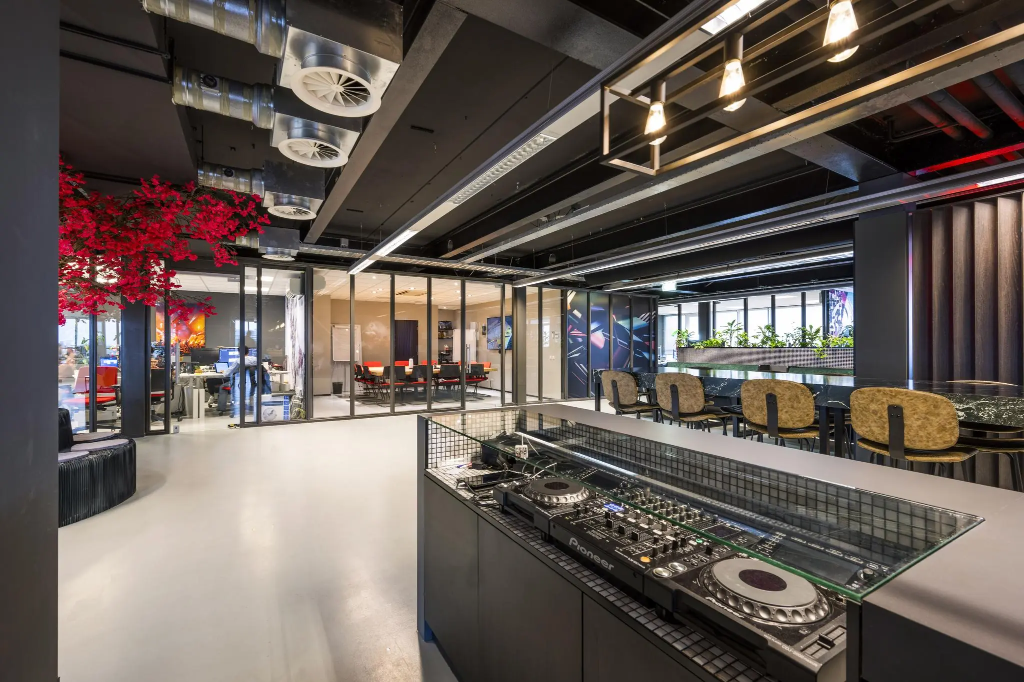 Moderne kantoorruimte aan de Anthony Fokkerweg met een glazen vergaderruimte, zithoeken, opvallende rode kunstboom en een DJ-booth op de voorgrond.